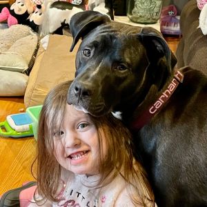 Ace is a black dog found as a sick puppy in Alabama and seen here resting his head on a young girl's head.